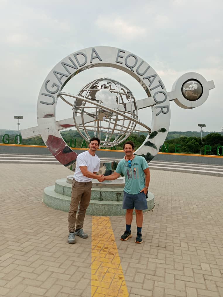 Two of Kelly's clients at the Uganda Equator monument, shaking hands at the line